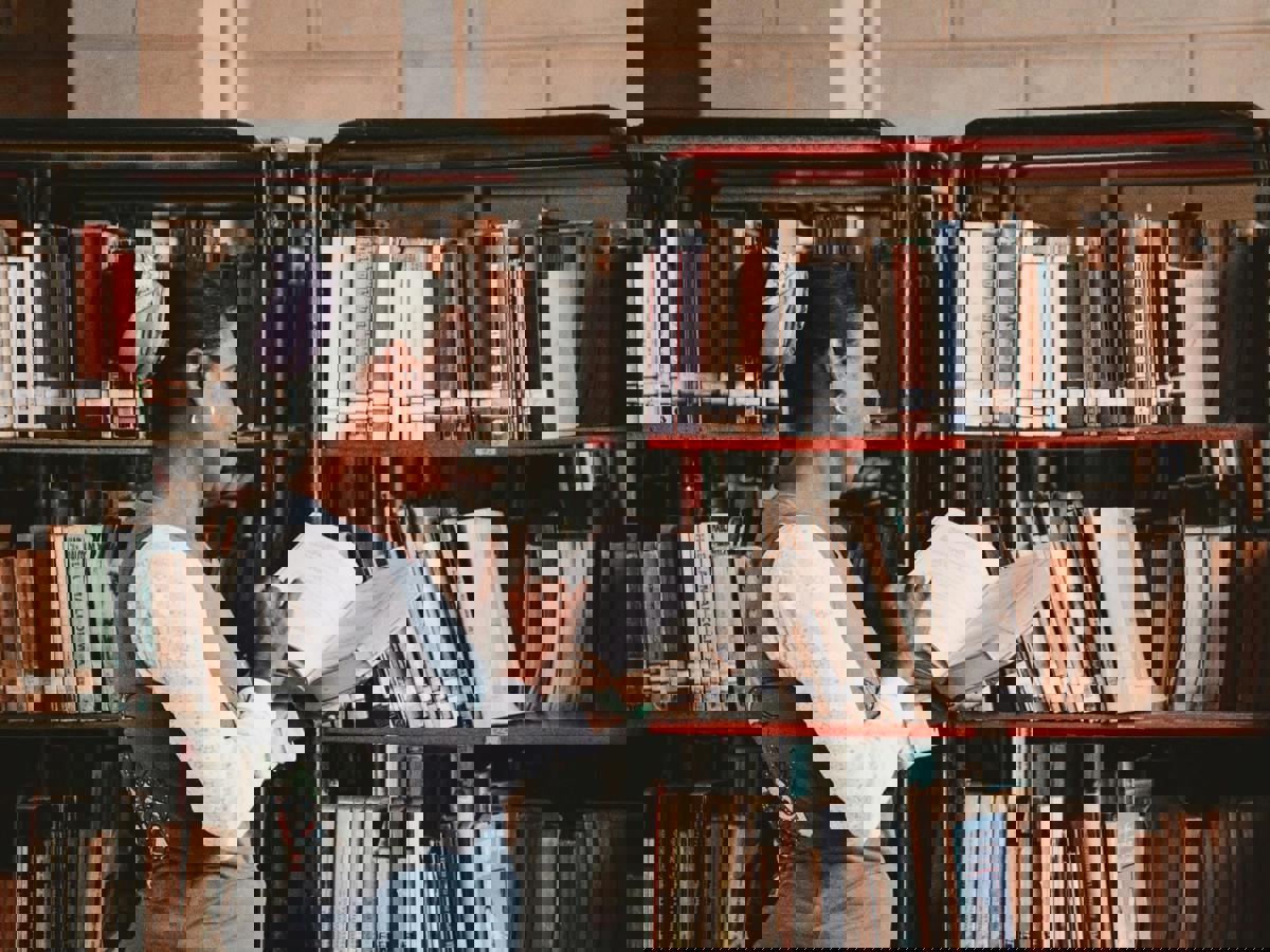Woman Looking Through a Book at the Library Bookcases